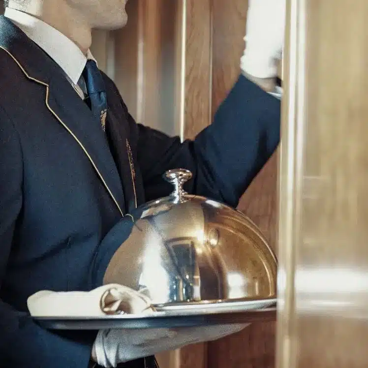 Service &agrave; la cloche d'argent par un membre d'&eacute;quipage en uniforme bleu marine du Transcant&aacute;brico Gran Lujo