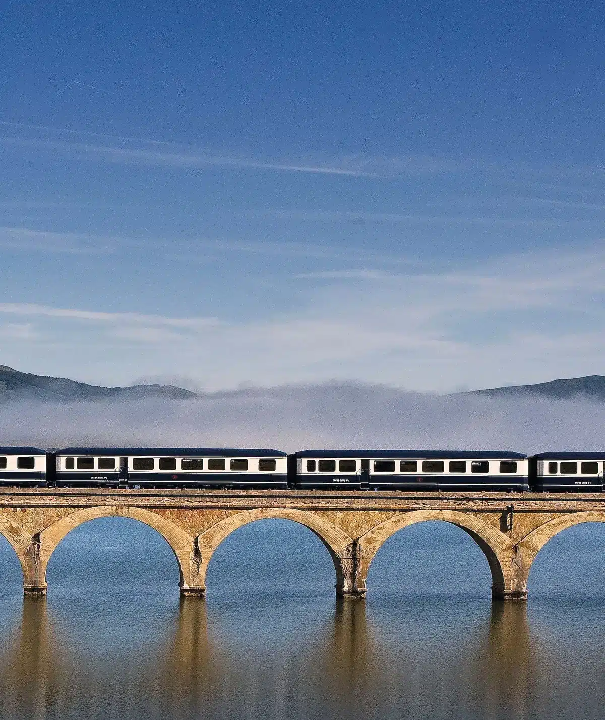 Train de luxe Transcant&aacute;brico Gran Lujo sur viaduc en arches de pierre refl&eacute;t&eacute; dans l'eau au lever du jour